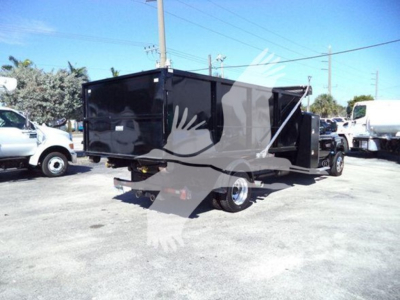 Truck: 2023 Chevrolet Silverado 6500HD roll-off body in an outdoor lot, black dump-style container, rear view showing dual wheels and hitch.