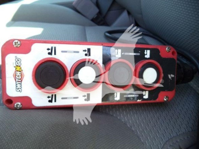 Control panel with red housing showing three circular ports and switch labels, likely a Switch-N-Go control module mounted in a vehicle seat area.