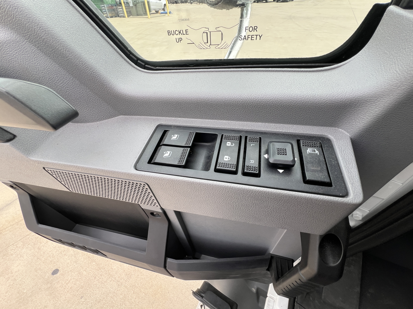 Cab interior switch panel of a 2027 Mack GR64B truck showing window/lock controls and dash area, near the driver door.