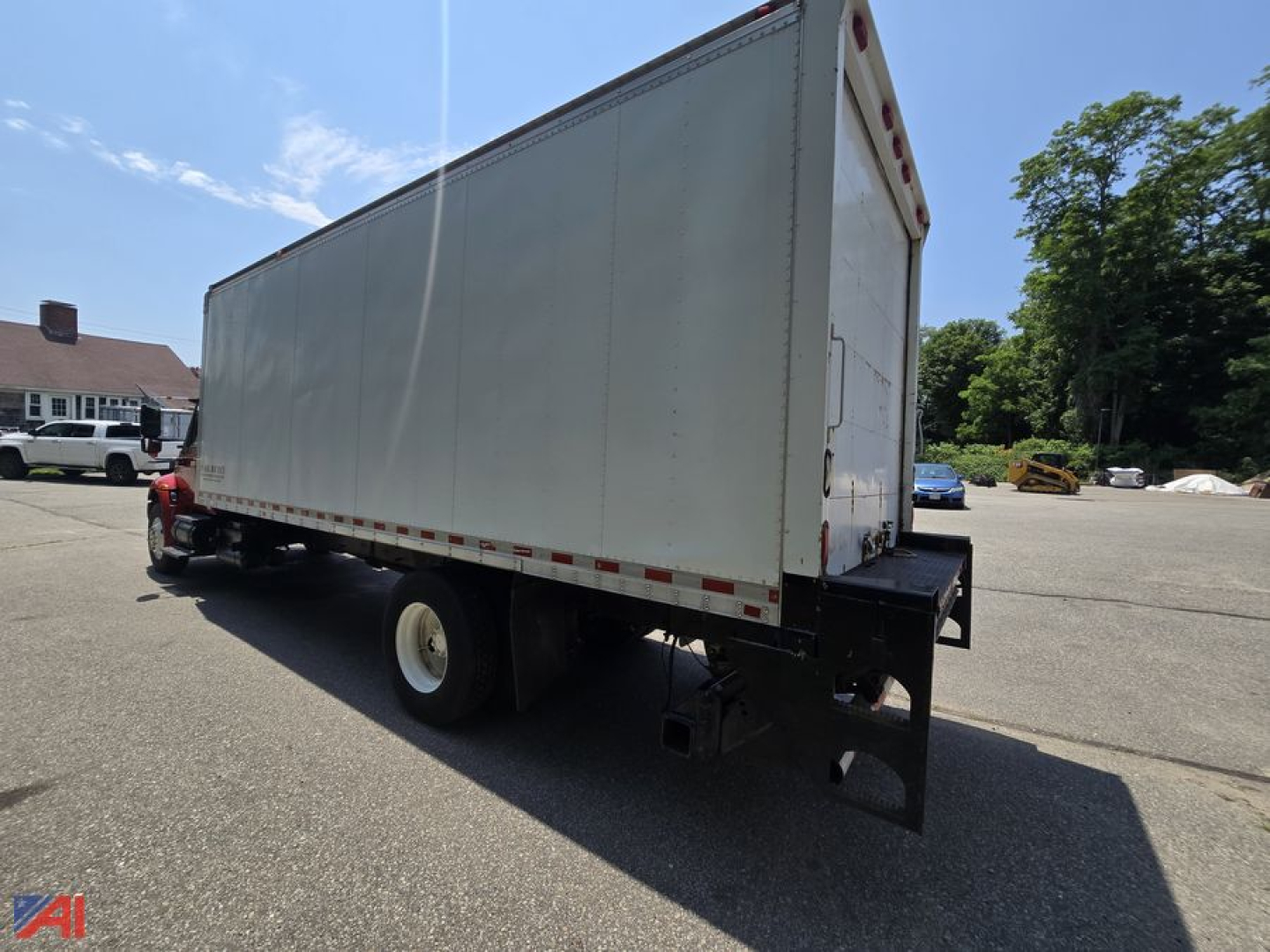 Box truck with a white cargo box mounted on a red cab. Side view showing the rear, with a black bumper and undercarriage, and a blue sky.
