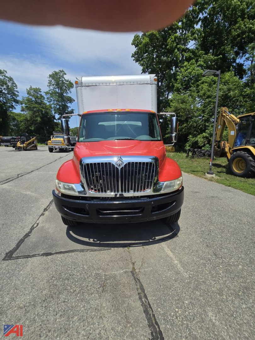 Box truck front view showing red cab, large chrome grille, and box behind cab.