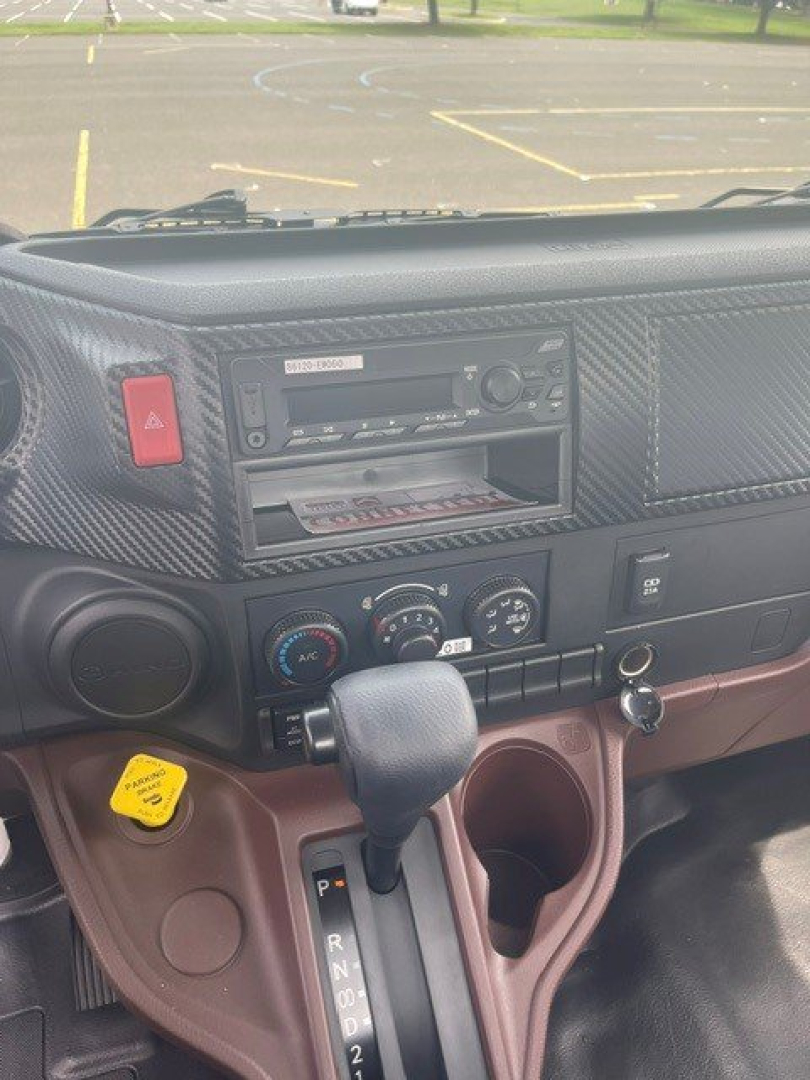 Dashboard of a new 2027 Hino L6 cab chassis showing gear selector in center, red hazard button, climate controls, and radio slot.