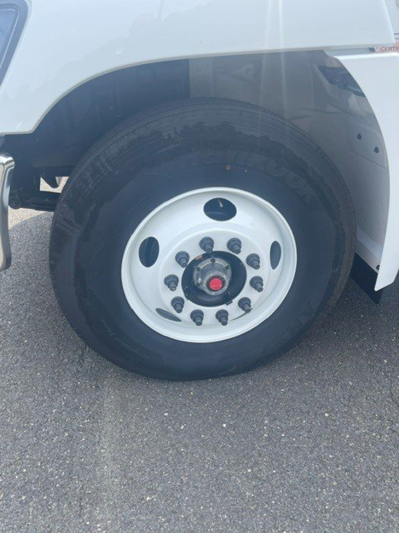 Front wheel of a truck showing large white steel rim with black lug nuts and a red center cap. Partial fender and wheel well visible.