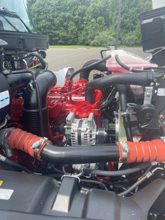 Hino L6 cab chassis engine bay with red engine components and black hoses. Visible alternator, hoses, and radiator reservoir.
