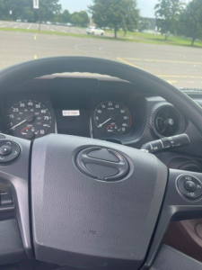 Cab interior of a 2027 Hino L6 truck showing steering wheel with Hino emblem, dashboard gauges, and control stalks.