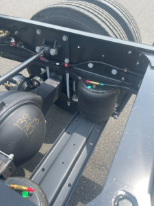 Truck chassis showing air reservoirs and hydraulic lines with visible labels; handwritten markings on an air tank reading '134 135' and various hoses and fittings.