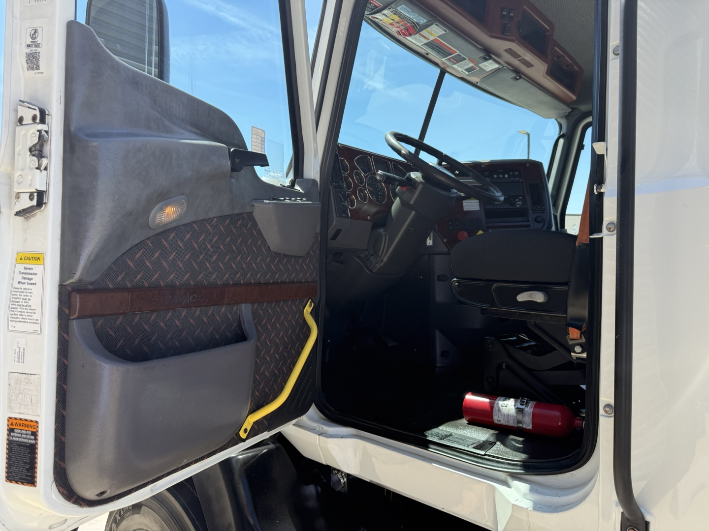 Truck cab interior view from open door showing steering wheel dashboard seats and entry step of a Mack CXU612 conventional daycab.