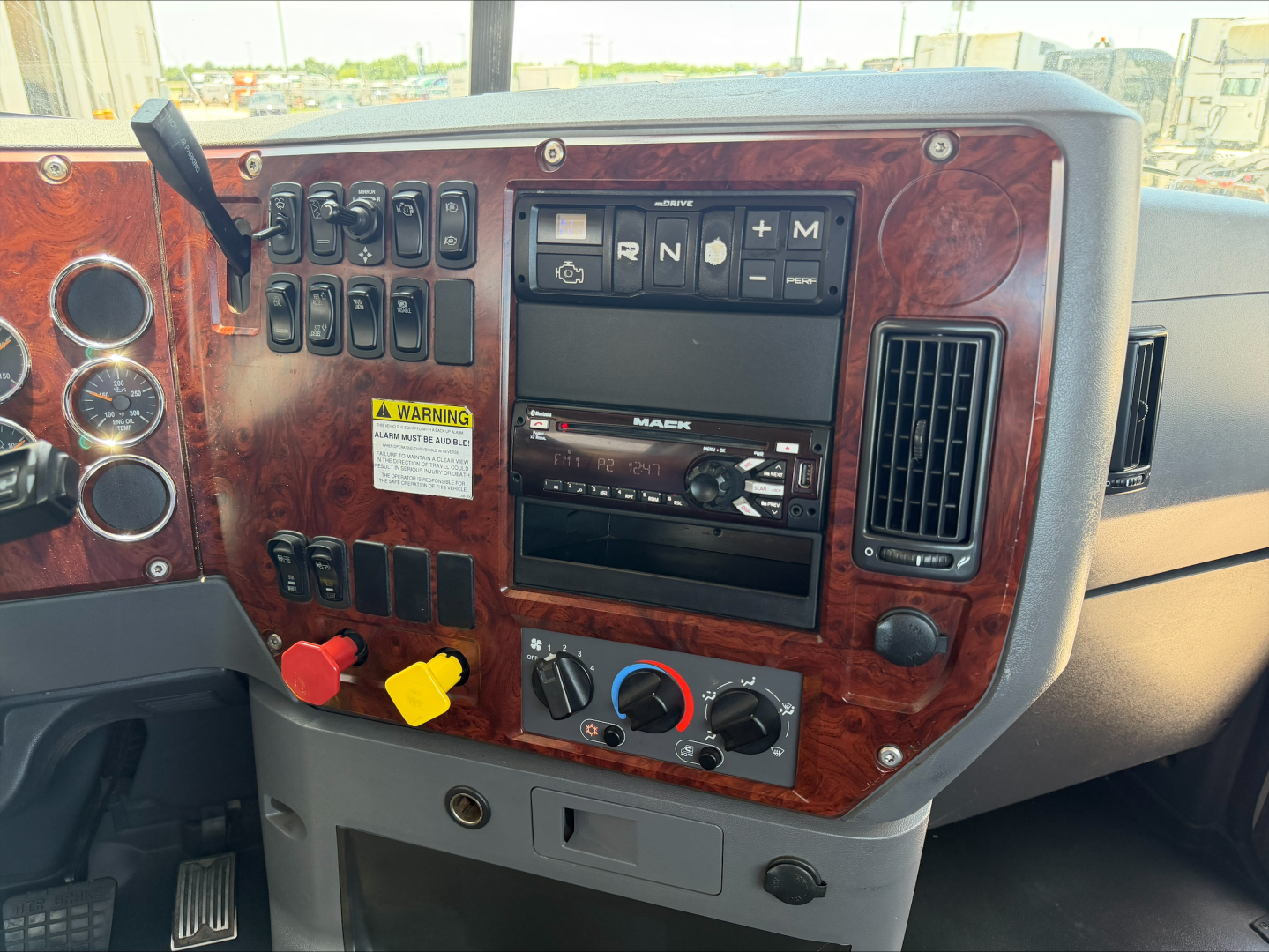 Dashboard of a 2018 Mack CXU612 showing gear selector, climate controls, and wood-grain panel with switches and a stereo unit.