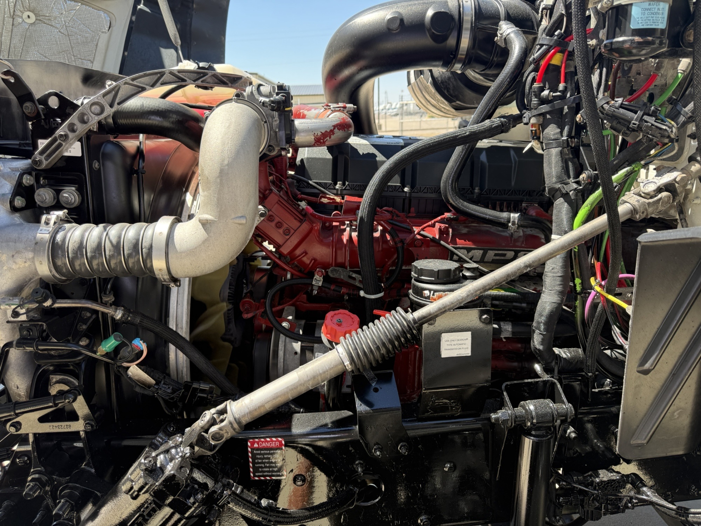 Truck engine bay of a 2018 Mack CXU612 with visible red engine, hoses, and components; cab area and wiring harnesses visible.