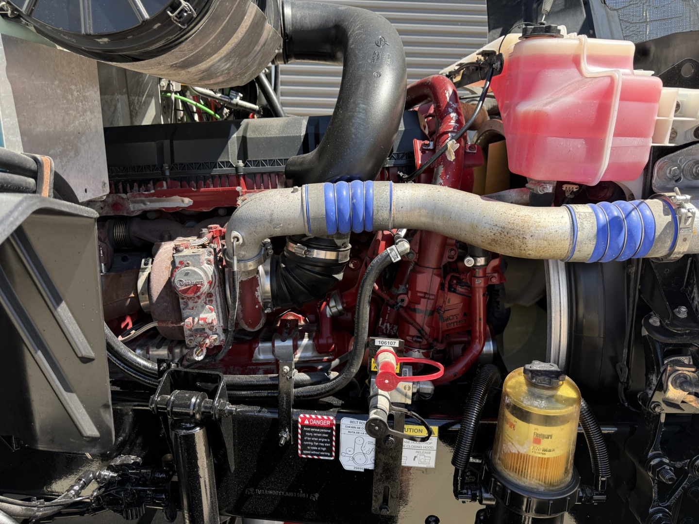 Mack CXU612 engine bay showing red engine block, vacuum hoses, coolant reservoir, and yellow hydraulic fluid filter canister.