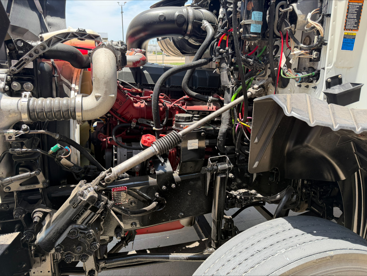 Mack CXU612 engine bay view showing complex hoses, cables, and engine components with red engine block and surrounding black metal framework.