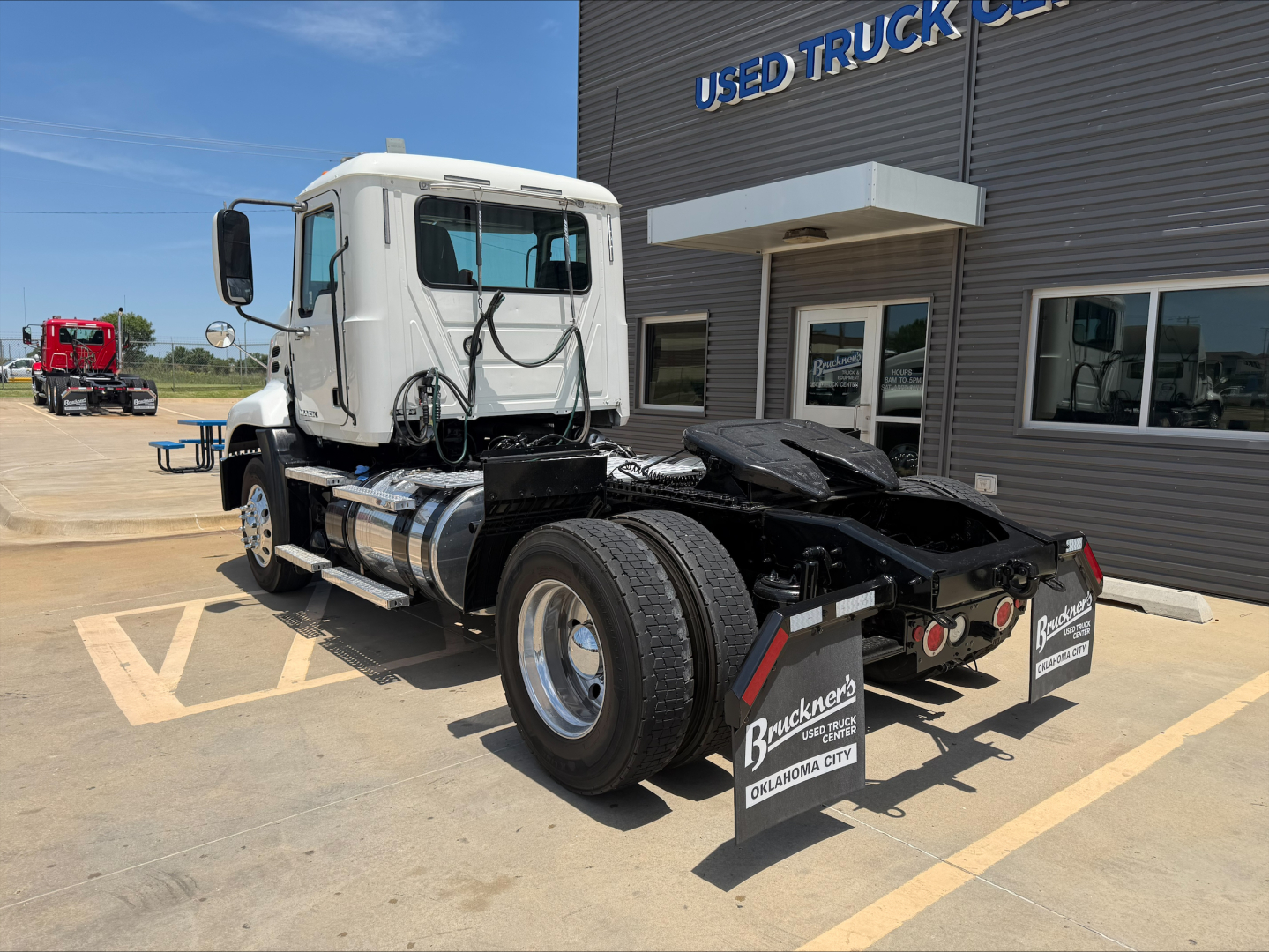 Truck chassis and cab of a white 2018 Mack CXU612 daycab seen from rear-right in a dealership lot.