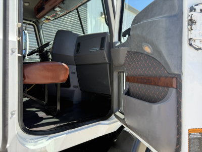 Cab interior of a 2018 Mack CXU612 daycab showing driver seat, steering wheel, dashboard, and open door with diamond plate panel.