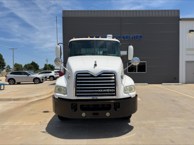 Front view of a white 2018 Mack CXU612 daycab truck with large chrome grille and bumper, parked in lot in front of dark gray building.