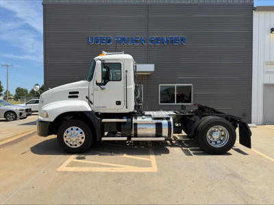 2018 Mack CXU612 conventional daycab truck side profile showing cab, chassis, fuel tanks, and wheels in front of a building with USED TRUCK CENTER signage.