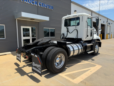 Truck cab and chassis showing Mack CXU612 with fuel tanks and rear view; front of a white daycab on a used truck lot.
