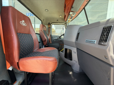 Truck cab interior showing driver's seat and passenger seat with red upholstery; dashboard with Pinnacle badge on glove compartment; overhead console and window; general cab interior of a Mack CXU612.