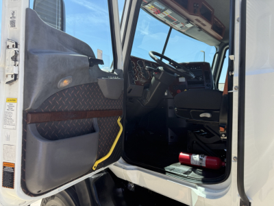 Truck cab interior view from open door showing steering wheel dashboard seats and entry step of a Mack CXU612 conventional daycab.