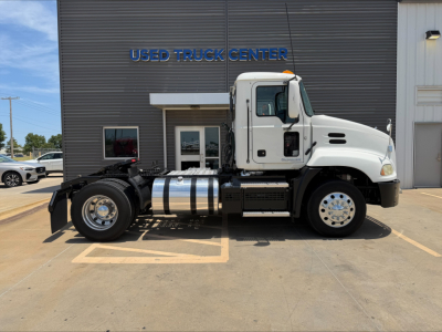 2018 Mack CXU612 daycab truck side view in front of a used truck center building; visible text includes USED TRUCK CENTER on the building sign; chrome fuel tank and wheels visible.