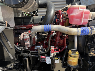 Mack CXU612 engine bay showing red engine block, vacuum hoses, coolant reservoir, and yellow hydraulic fluid filter canister.