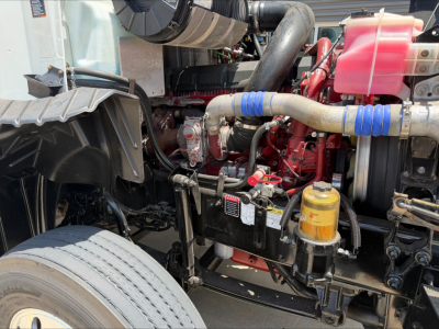 Mack CXU612 engine bay showing coolant reservoir, hoses, yellow oil filter, and red engine block with blue hose sleeves.