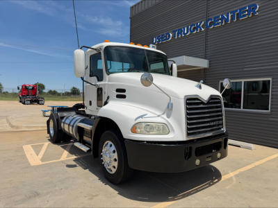 White 2018 Mack CXU612 daycab truck front-left view with large grille, side mirrors, and fuel tanks. Truck is parked in lot near used truck center building.