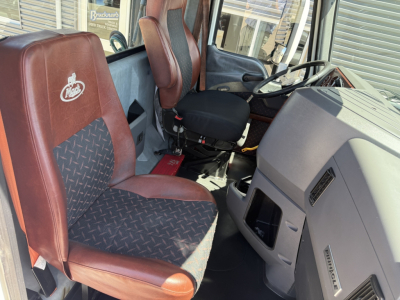 Cab interior of 2018 Mack CXU612 truck showing driver seat with brown fabric, red piping, and Mack logo, steering wheel, dash, and passenger seat.