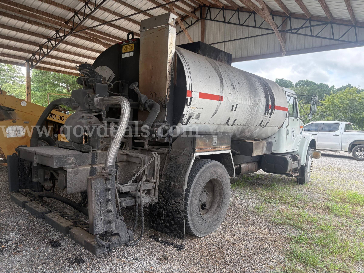 Rear view of an International 4900 asphalt/spread truck with a large cylindrical tank and vacuum pump components visible.