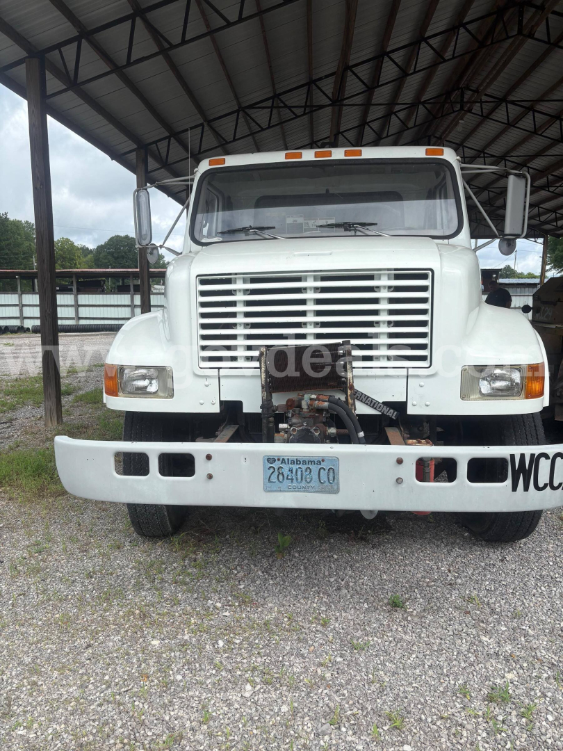 Truck front view of a white 1998 International 4900 with large grille, bumper, and towing apparatus visible in a gravel lot.