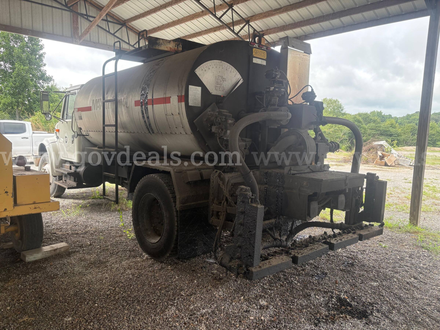 Rear view of a black-and-silver International 4900 vacuum/tanker truck with a cylindrical tank and hose assembly, under a metal shelter.