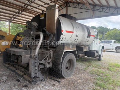 Rear view of an International 4900 asphalt/spread truck with a large cylindrical tank and vacuum pump components visible.
