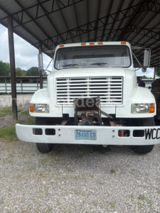 Truck front view of a white 1998 International 4900 with large grille, bumper, and towing apparatus visible in a gravel lot.