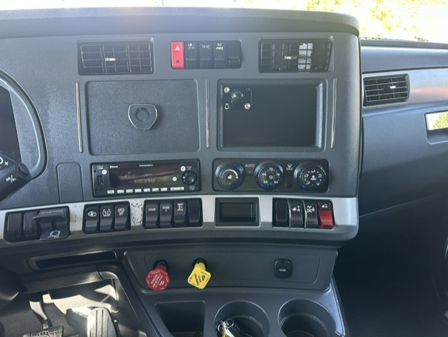 Kenworth T680 dash panel showing control switches, vents, climate controls, ignition area, and cup holders.