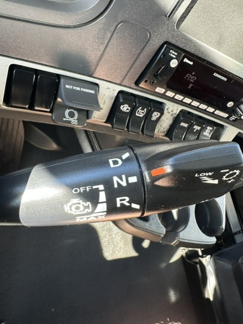 Kenworth truck interior with gear selector showing P R N D positions and auxiliary controls; dashboard switches and a Kenworth electronics unit visible.