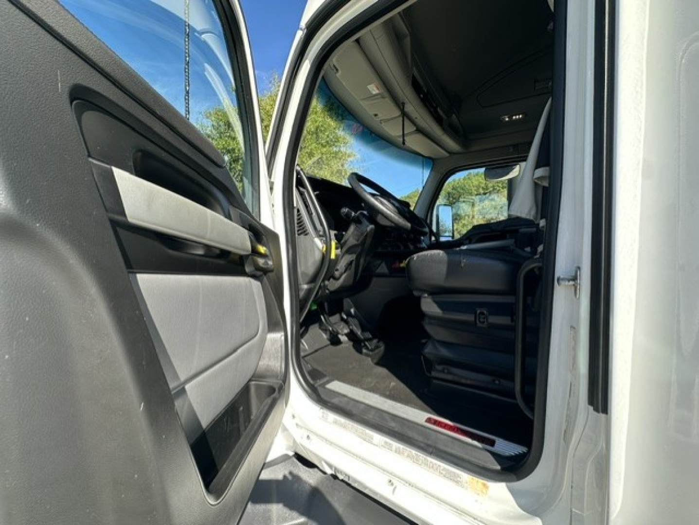 Interior view of a Kenworth truck cab with open door, showing driver's seat and dashboard area.