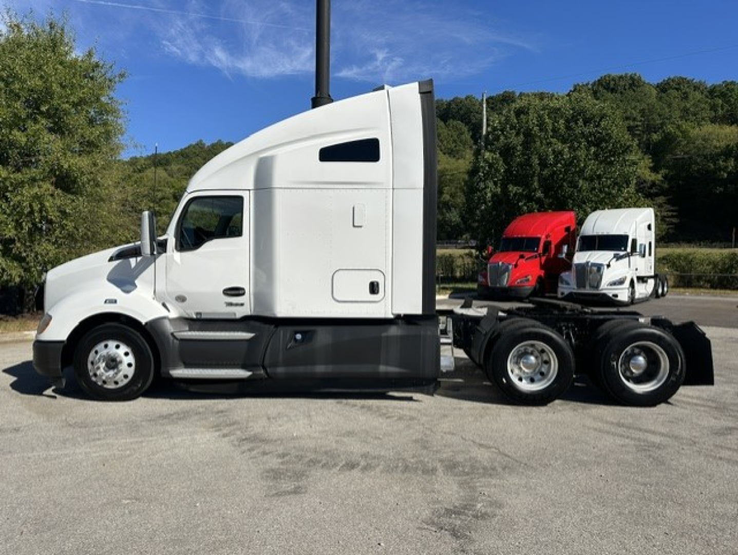 Kenworth T680 tractor side view showing cab with sleeper, chassis, dual rear axles, and two additional trucks in background.