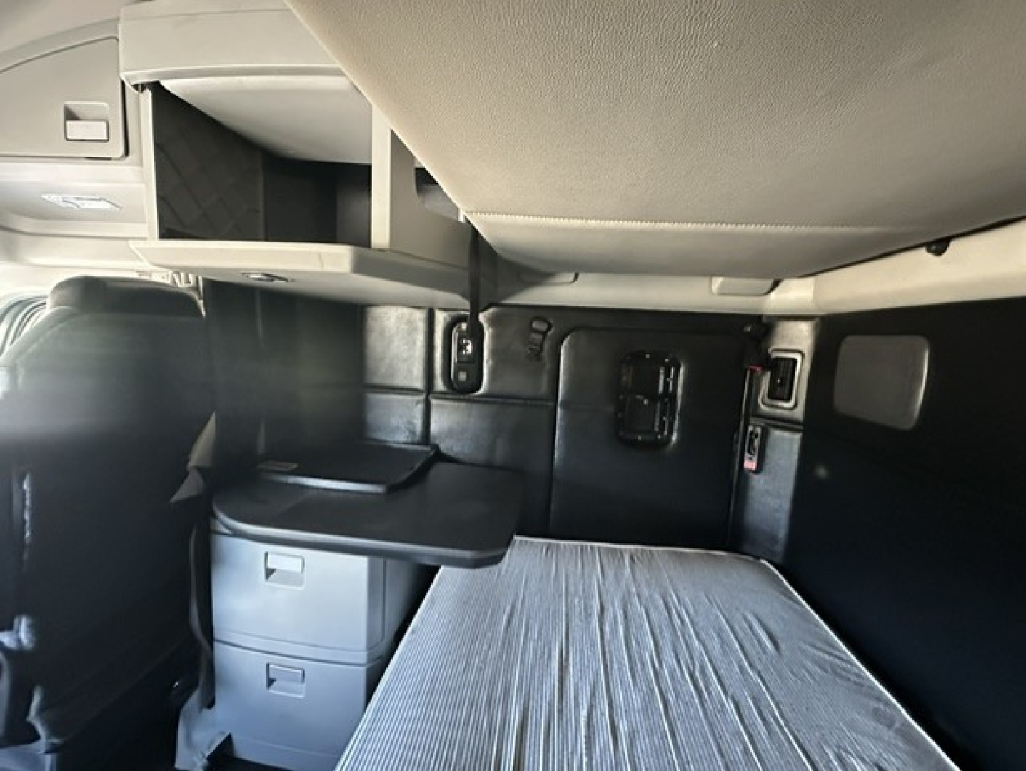 Kenworth T680 sleeper cab interior showing bunk bed with mattress, storage drawers, and overhead shelf.