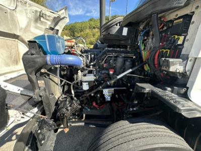 Kenworth T680 engine bay with exposed cold air intake and wiring harnesses beneath open hood showing engine components.