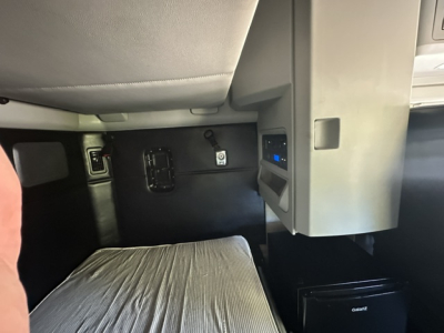 Kenworth T680 interior view showing dashboard pocket and controls near driver seat; small display panel; cab area with black panels and a sleeper area visible.