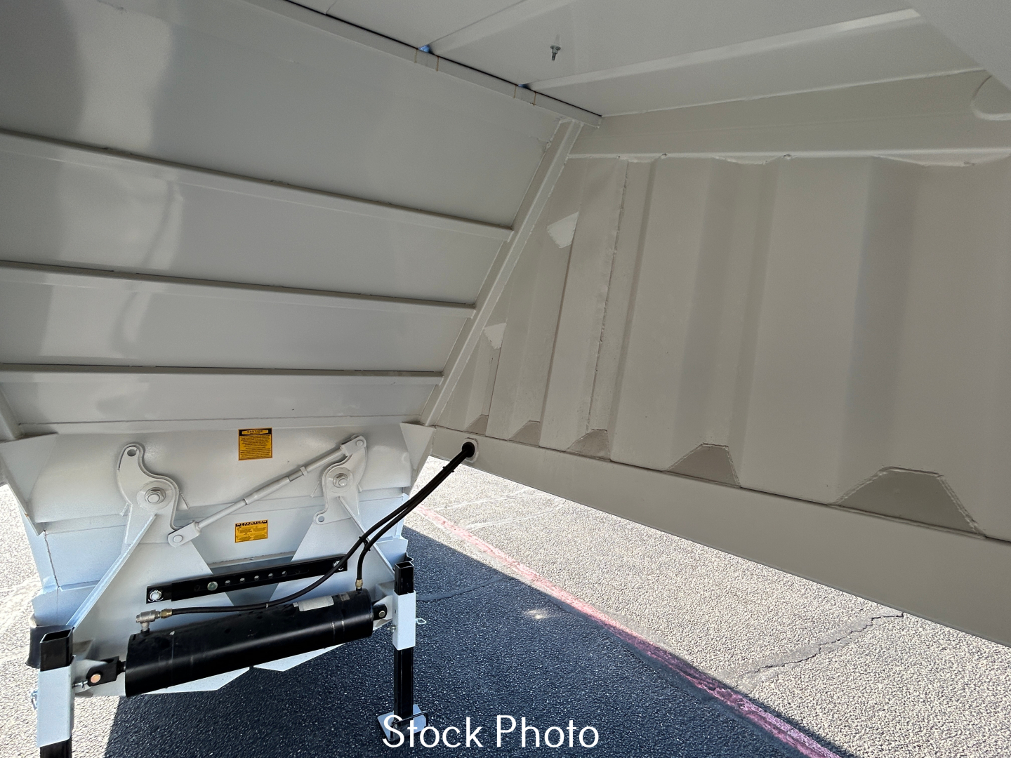 Dump trailer underside and hitch mechanism with hydraulic cylinder and support legs, light gray paint, angular sidewall paneling visible.