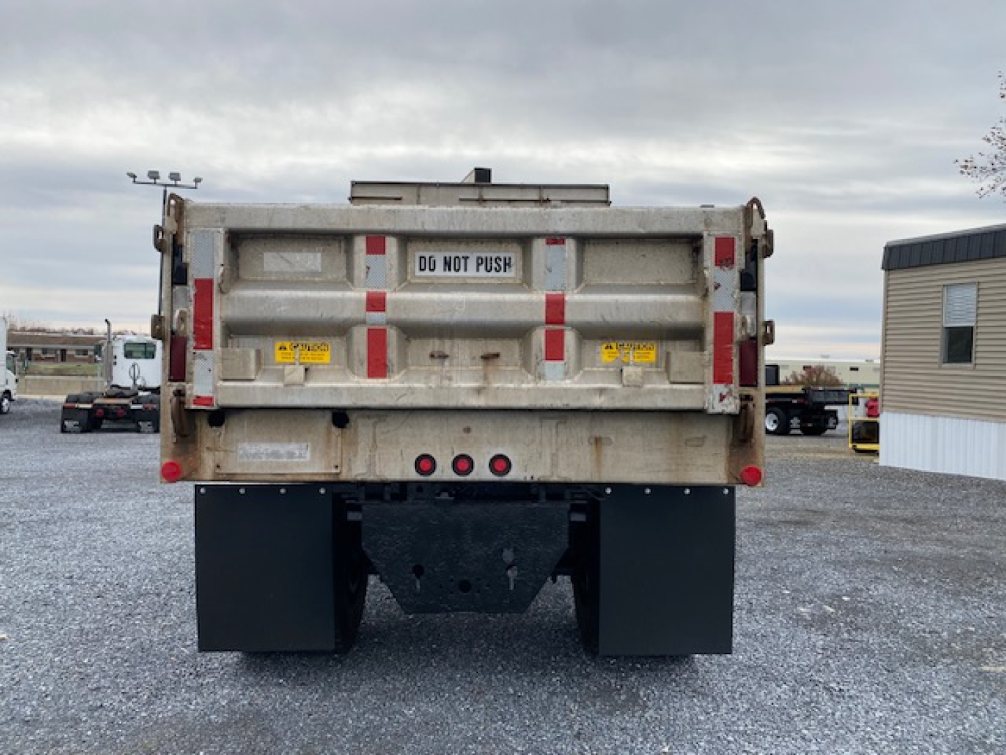 Dump truck rear showing DG NOT PUSH sign, taillights, and mud flaps in gravel lot.