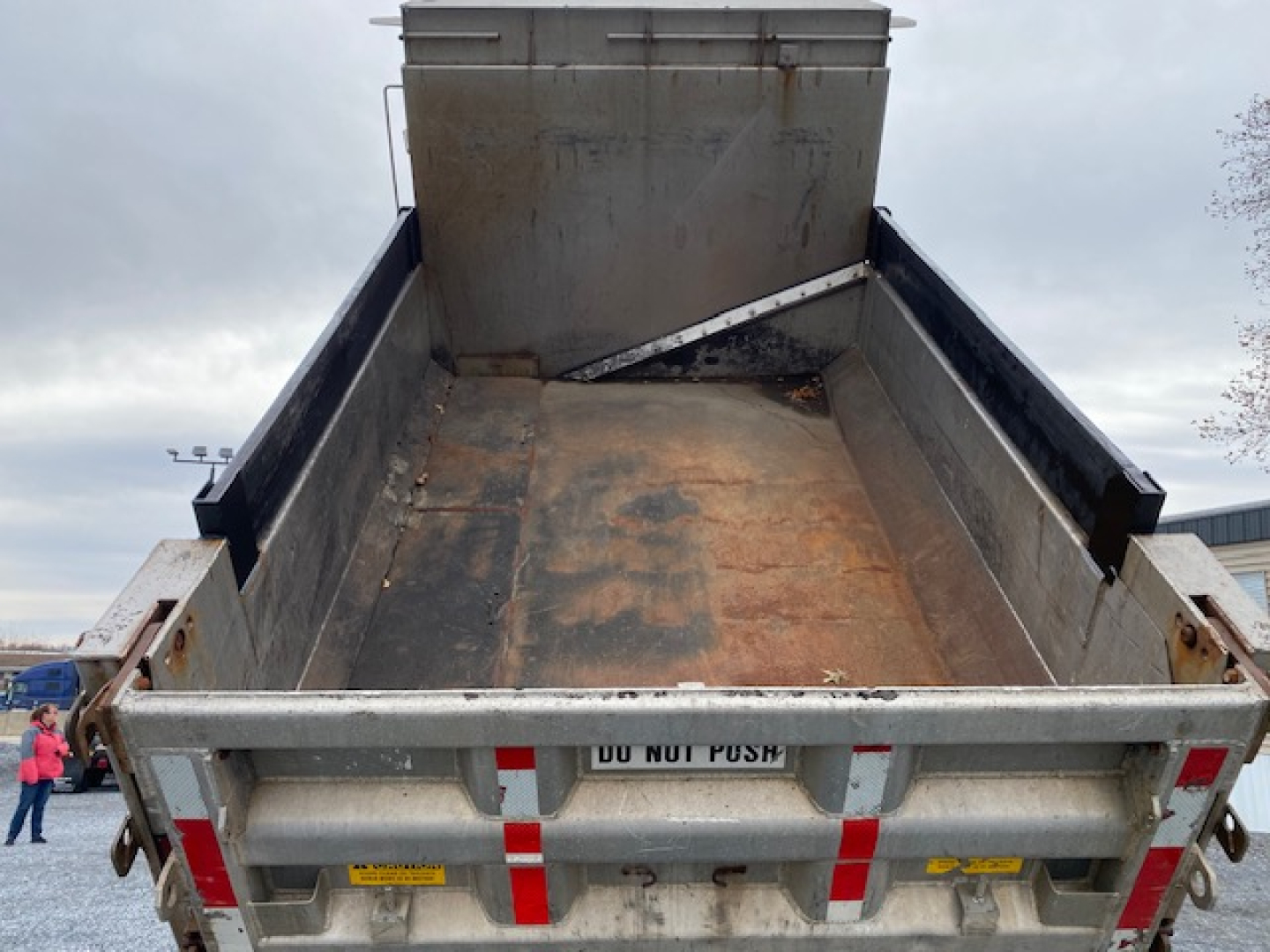 Dump truck bed of a 2007 International 7400 with open tailgate showing cargo bed and hydraulic mechanism, metal surface with wear.