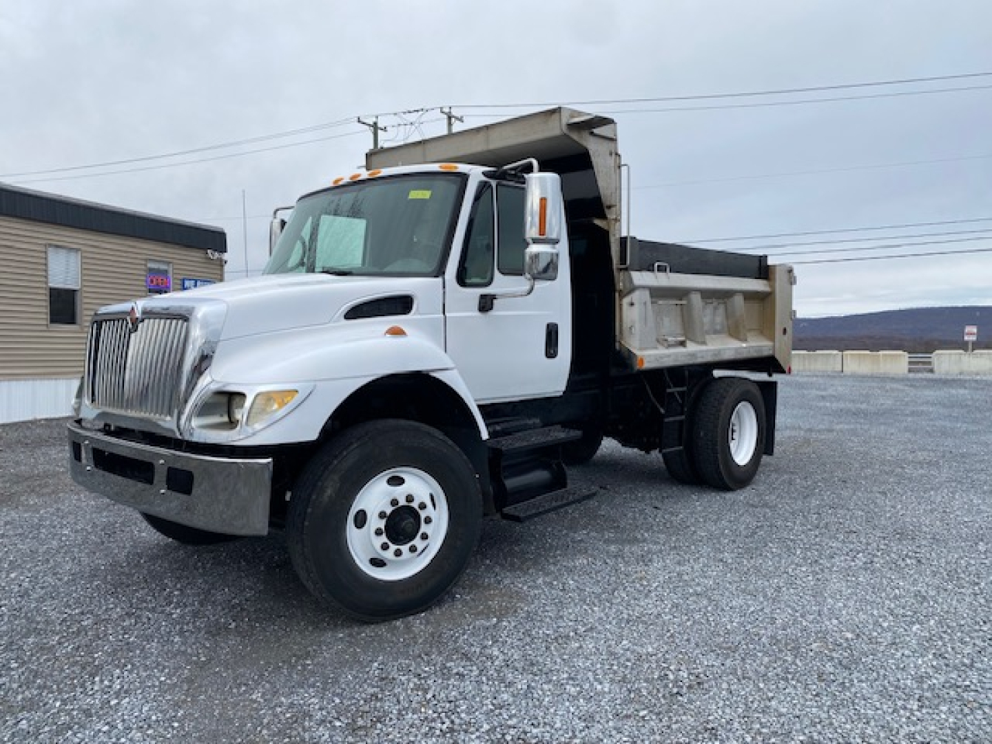 White 2007 International 7400 dump truck with dump bed open, front grille, large side mirrors, dual rear wheels, parked on gravel lot.