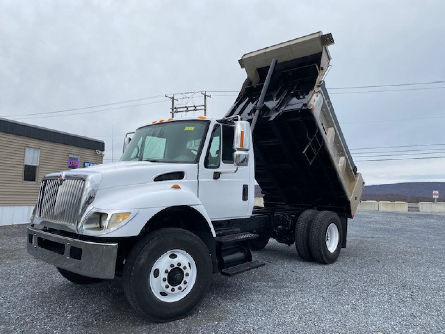 Truck cab and raised dump bed of a white 2007 International 7400 dump truck showing gull-wing bed raised for discharge.