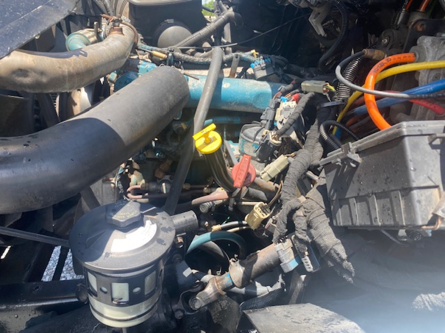 Truck engine bay of a 2007 International 7400 showing various hoses, wiring, yellow handle, and orange battery cables.