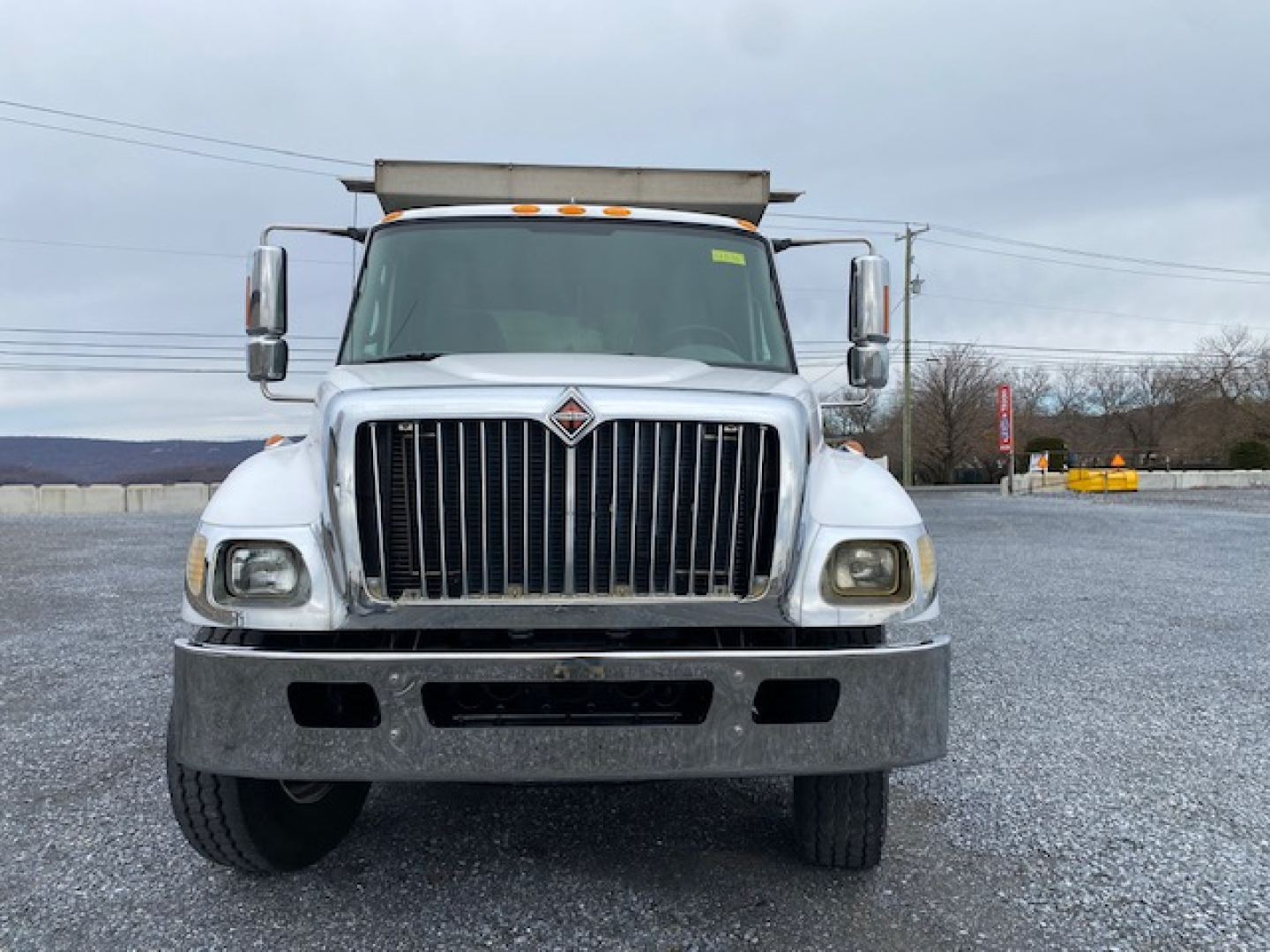 International 7400 dump truck front view showing grille, bumper, headlights, and large silver bumper in a gravel lot.