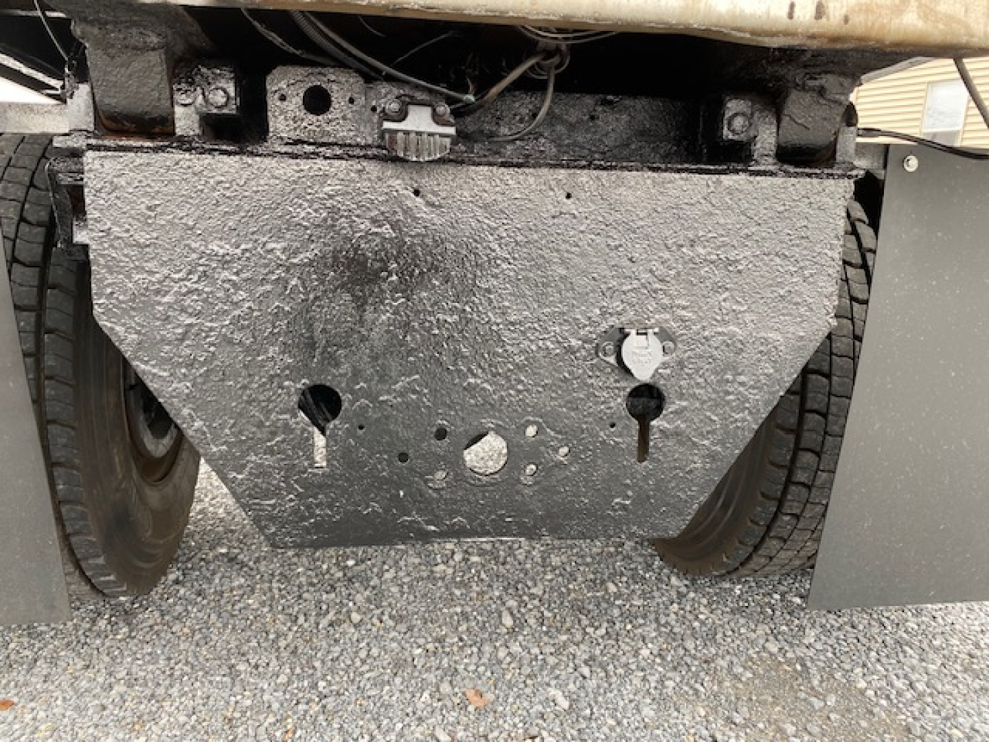 Truck undercarriage with a large textured metal skid plate between dual rear wheels, showing mounting holes and rough surface.