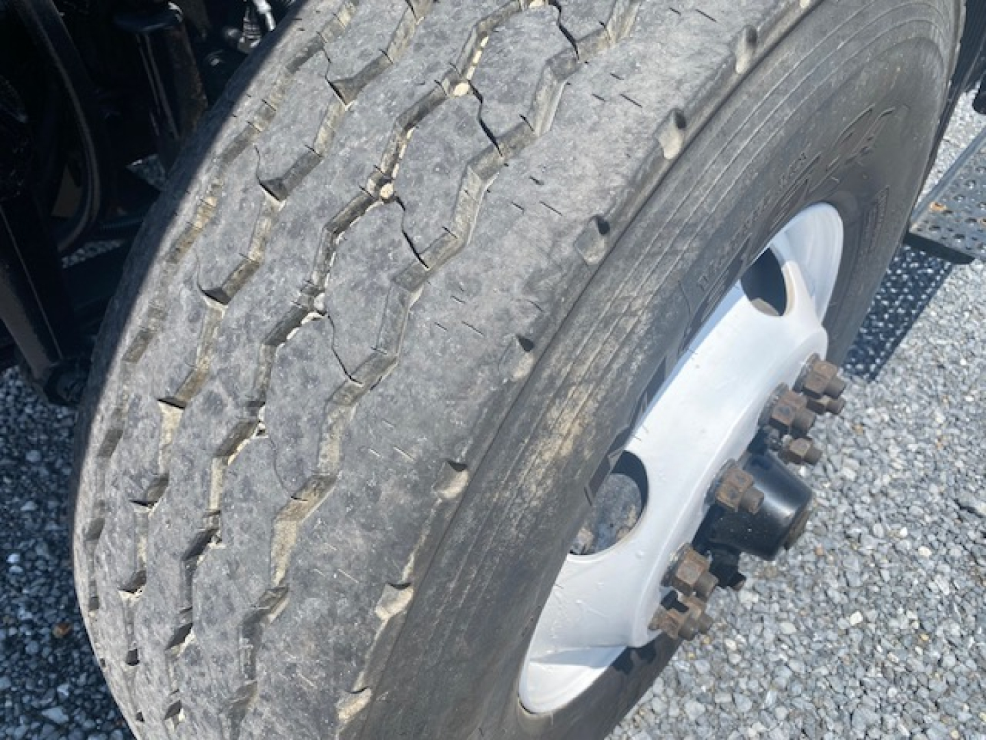 Truck wheel and tire close-up showing hub with lug nuts; tread pattern visible on tire; part of suspension and frame visible.