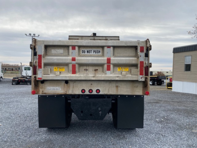 Dump truck rear showing DG NOT PUSH sign, taillights, and mud flaps in gravel lot.