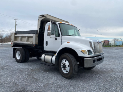Dump truck showing cab and dump bed, International branding, white cab with black chassis and dumping bed, front grille with chrome accents, side mirrors, and wheel wells.